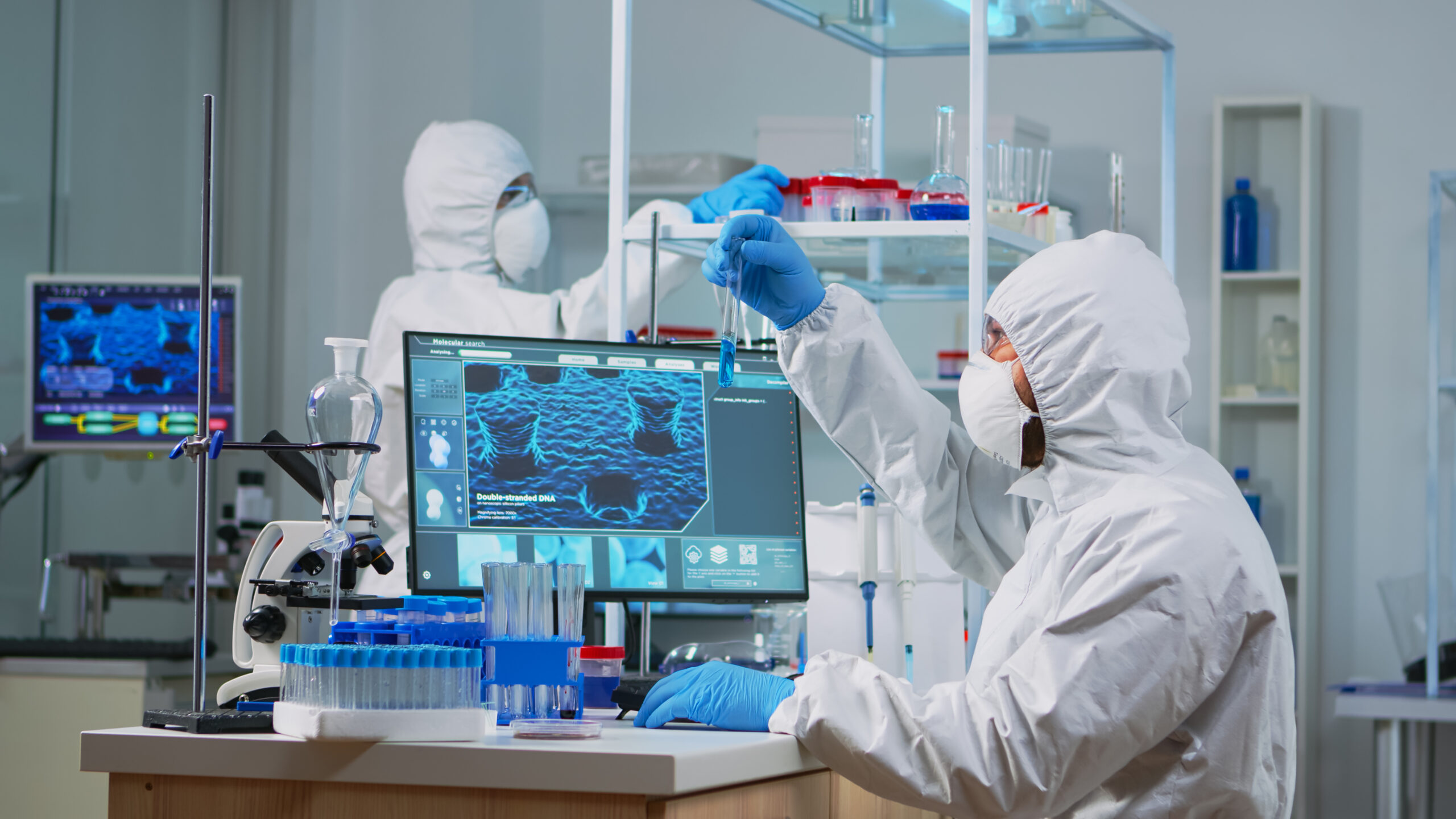 Neurologist with ppe suit working at vaccine development in equipped laboratory typing on pc. Team examining virus evolution using high tech for research in treatment development against covid19