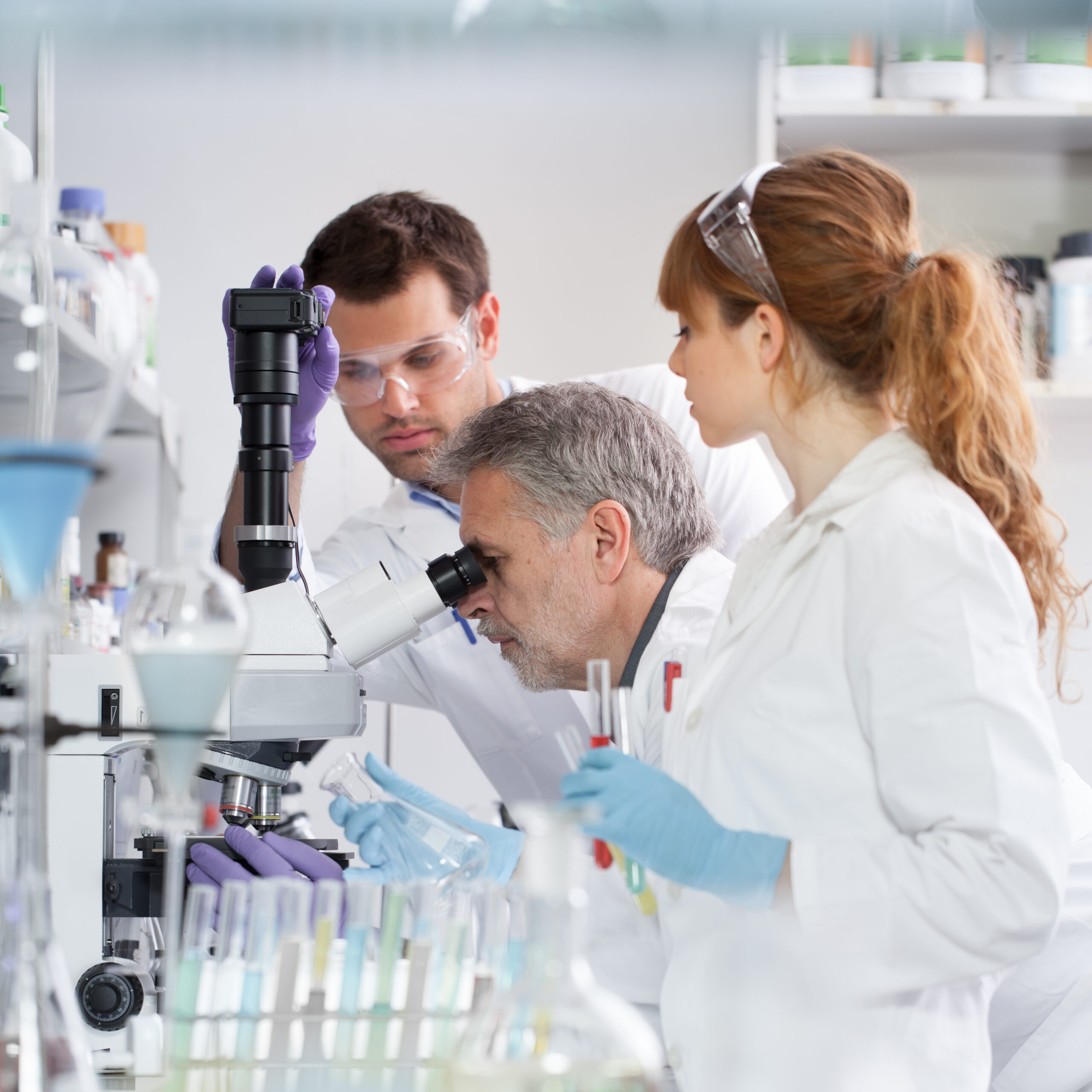 Health care researchers microscoping in life science laboratory. Young research scientists and senior professor preparing and analyzing microscope slides in research lab.